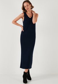 Abito maxi a coste navy con scollatura a V, senza maniche, fessure laterali e silhouette aderente, abbinato a stivali neri alla caviglia.