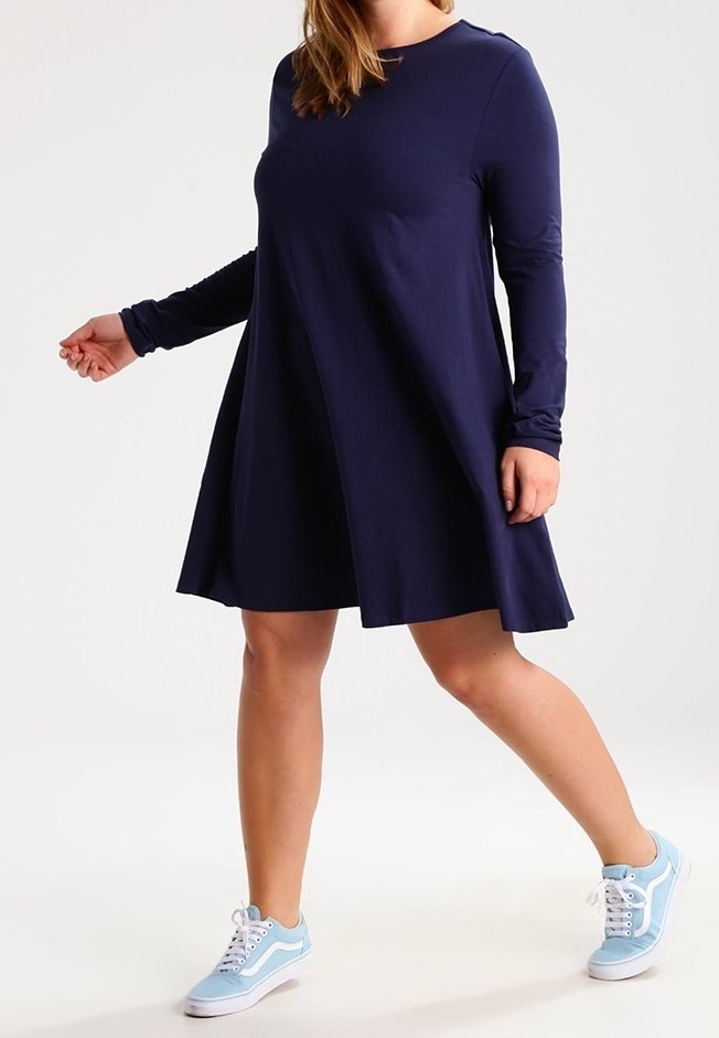 Granatowa sukienka z długim rękawem o luźnym kroju, rozkloszowanym spodzie i miękkiej fakturze. Noszona z jasnoniebieskimi trampkami.