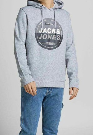 Felpa grigia con un logo circolare grafico frontale. Dotata di cappuccio con cordoncino, polsini a coste e una vestibilità comoda. Abbinata a jeans blu.