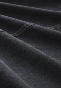 Nahaufnahme eines schwarzen Stoffes mit sichtbaren Nähten und weichen Falten, die die Textur und das Webmuster hervorheben.