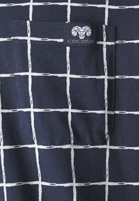 Marineblauer Stoff mit einem weißen Karomuster. Verfügt über eine kleine Tasche und ein Logo mit einem Widderkopf. Das Material wirkt weich und strukturiert.