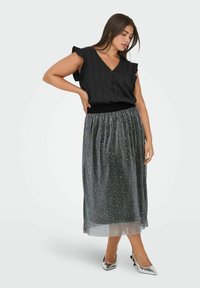 Blusa negra de escote en V con mangas con volantes, combinada con una falda larga plisada plateada con acentos metálicos dispersos y tacones plateados.