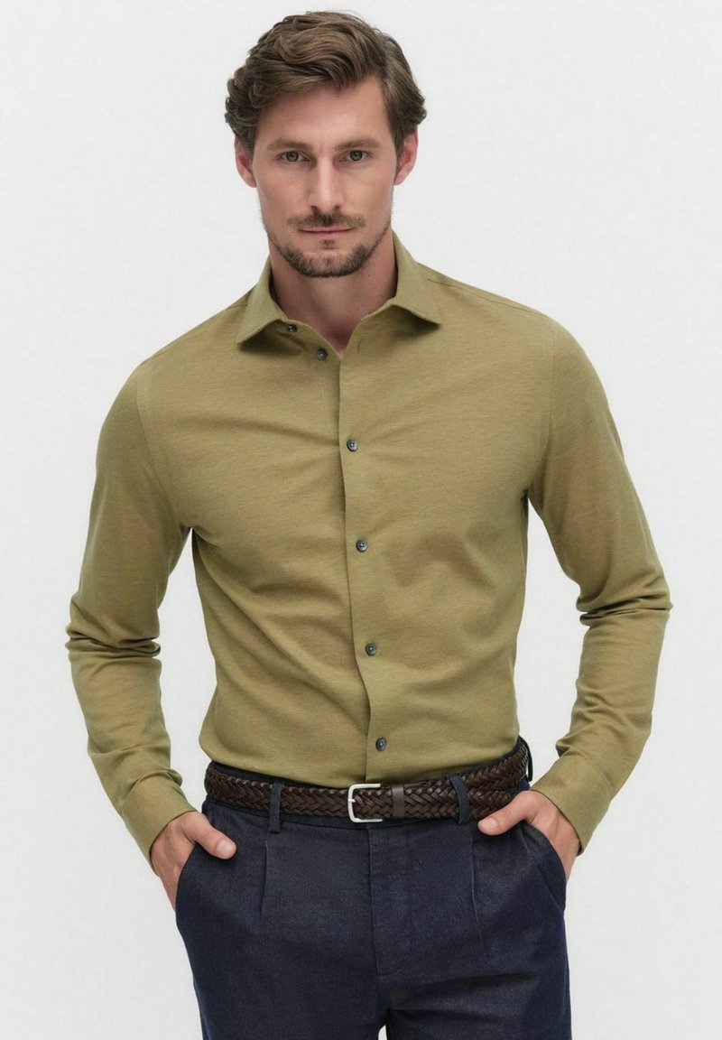 Olijfgroene overhemd met lange mouwen en knopen, gladde textuur, en een puntige kraag, gecombineerd met een gevlochten bruine riem en donkere broek.
