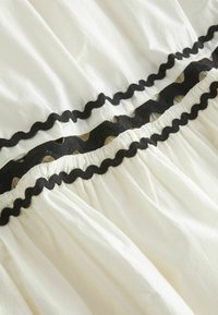 Biele tkaniny s čiernym ozdobným lemovaním. Textil má hladkú textúru a zhluky na spodnej strane.