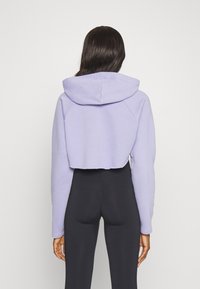 Felpa corta in morbido tessuto lavanda, con cappuccio attaccato, maniche raglan e orlo grezzo. Indossata sopra leggings neri.