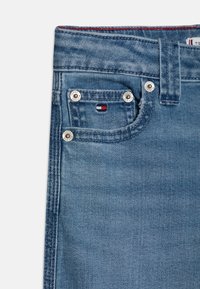 Ανοιχτό γαλάζιο τζιν παντελόνι με σχέδιο πέντε τσεπών, που διαθέτει ασημένια εξαρτήματα, κόκκινες ραφές και μία μικρή ετικέτα λογότυπου κοντά στην τσέπη.