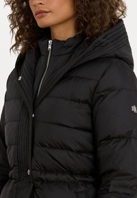 Μαύρο μπουφάν με επένδυση, με ψηλό γιακά, οριζόντια ραμμένη υφή, φερμουάρ και μεταλλικό λογότυπο στον ώμο.