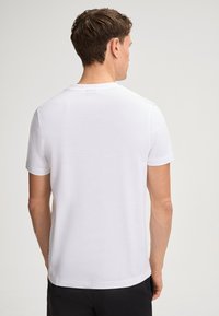 White short-sleeve t-shirt with a round neckline and a smooth texture. Simple design with a straight cut, worn with dark pants.