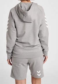 Sudadera gris con cordón y logo en la parte posterior, combinada con pantalones cortos grises que tienen acentos en chevron blancos en el lateral. Tejido suave y texturizado.