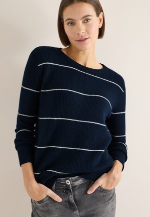 Maglione a righe navy con linee orizzontali bianche, texture a coste, scollo rotondo e maniche lunghe, abbinato a jeans grigi.