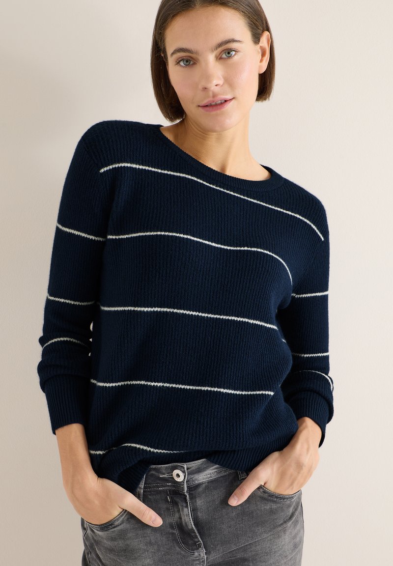 Navy striped sweater with white horizontal lines, ribbed texture, round neckline, and long sleeves, paired with grey jeans.