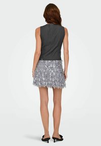 Pelēks bezroku tops, kombinēts ar sudraba krāsas bārkstainu svārku ar spīdumiem, kam ir teksturēta apdare un piegulošs siluets.