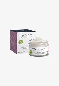 Crema anti-imperfezioni Teaology Tea Glow in un barattolo trasparente con una crema bianca all'interno, accompagnata da una scatola viola e nera, formato 50 ml.