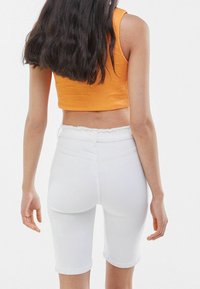Pantalones cortos de mezclilla blanca con dobladillo deshilachado, combinados con un top corto sin mangas de color naranja texturizado. Diseño simple y ajustado.