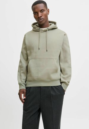 Olijfgroene hoodie van zachte stof, met een voorzak, kap met trekkoord en ribgebreide manchetten. Gecombineerd met antracietgrijze broeken.