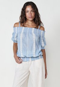 Blusa azzurro chiaro off-the-shoulder realizzata in tessuto morbido con dettagli ricamati bianchi, maniche a sbuffo e orlo inferiore arricciato.