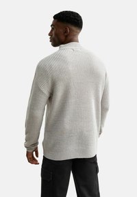 Suéter de punto gris claro con textura acanalada, cuello redondo y costuras de hombro caídas, combinado con pantalones cargo negros.
