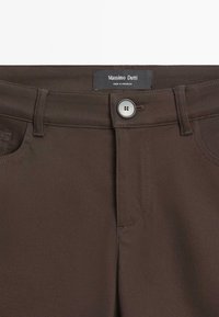 Tmavě hnědé kalhoty s předním knoflíkem a zipem, poutky na pásek a štítkem s nápisem „Massimo Dutti Made in Morocco“ uvnitř pásku v pase.
