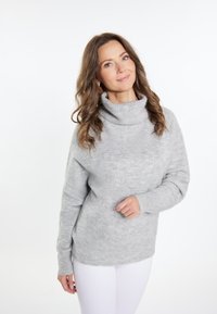 Grijze coltrui gemaakt van ribbelstof, met lange mouwen en een relaxte pasvorm, gecombineerd met witte broek.