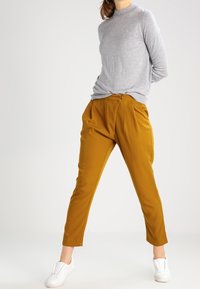 Grå långärmad tröja i kombination med senapsgula tapered-byxor; outfiten har en avslappnad passform och mjukt tyg; fulländad med vita sneakers.