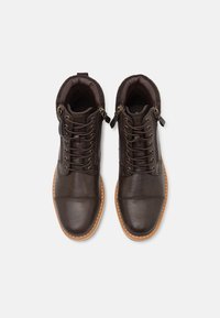Brown leather ankle boots with rounded toe, lace-up front, side zippers, and faux fur lining. Contrasting tan sole.