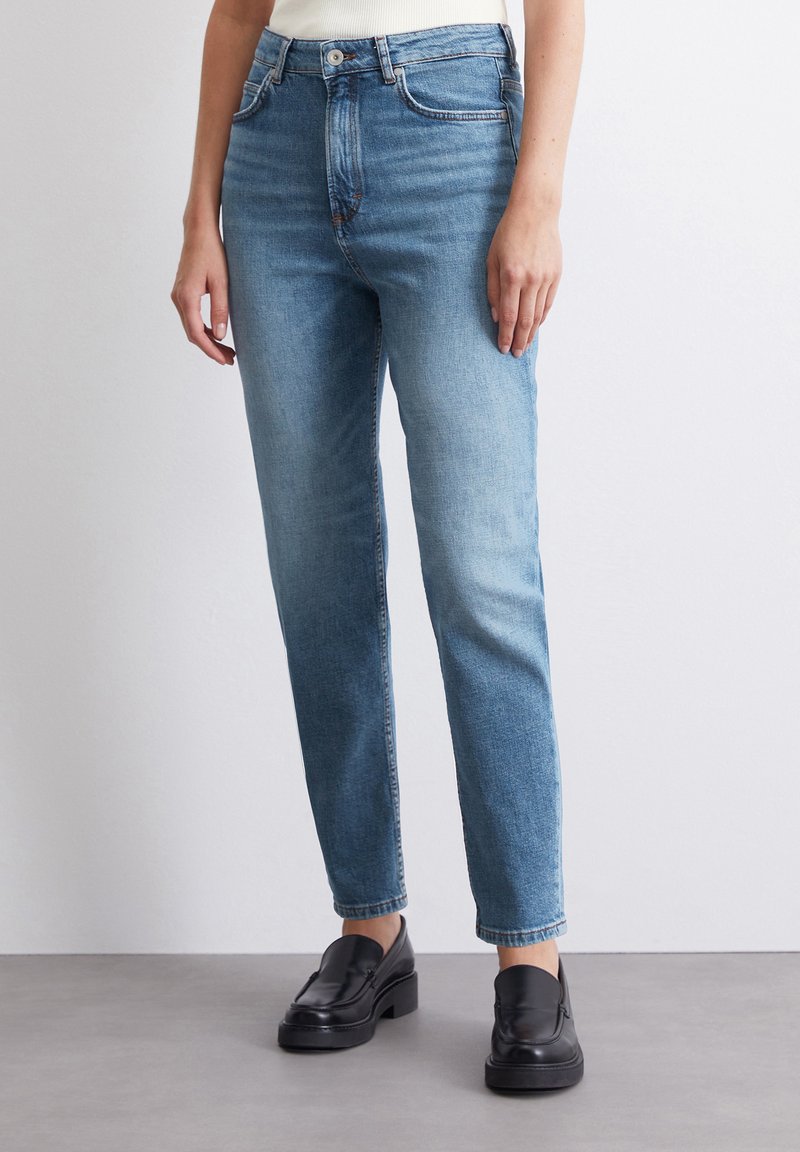Light blue denim jeans with a straight leg cut, five pockets, and slight fading. Worn with black loafers, featuring a textured finish.