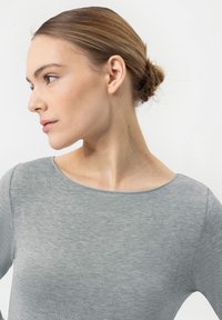 Haut gris à manches longues avec un col rond, texture douce et design ajusté, présenté sur un modèle avec les cheveux coiffés en chignon.