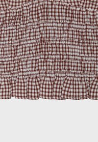 Gros plan d’un tissu à carreaux marron et blanc avec des sections froncées et élastiquées créant un motif texturé plissé et un ourlet à volant.