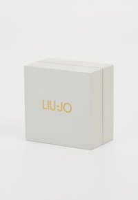 Balts tekstūrēts kastīte ar zelta "LIU·JO" logo priekšpusē. Kvadrātveida forma ar tīru, minimālu dizainu.