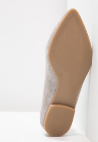 Grijze suède hoge hak schoen vanuit de achterkant bekeken, met een beige zool en een maatlabel, tegen een witte achtergrond.