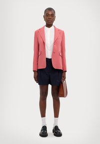 Pink tailored blazer over a white shirt, paired with navy shorts. Black platform shoes and a brown handbag complete the look.