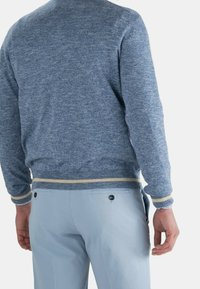 Pull bleu tricoté avec un mélange de textures, comprenant des poignets et un ourlet côtelés avec des accents jaune clair, associé à un pantalon bleu clair.