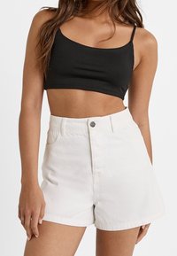 Top corto nero con spalline sottili abbinato a pantaloni shorts bianchi in denim a vita alta, con tasche frontali e chiusura a un solo bottone.