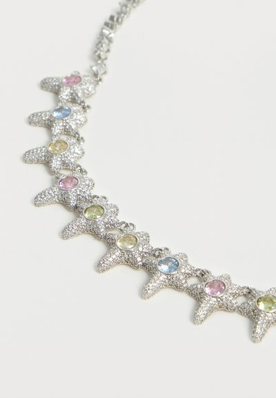 Ασημένιο κολιέ αστερίας με εναλλασσόμενες παστέλ πολύτιμες πέτρες σε ροζ, μπλε, κίτρινο και πράσινο σε λευκό φόντο.