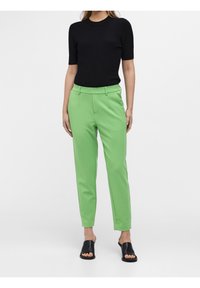 Haut noir côtelé à manches courtes et pantalon vert ajusté à texture lisse, avec une taille cintrée et des poches latérales. Sandales noires à enfiler.