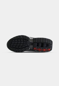 Semelle de basket noire avec une bande de roulement texturée, des détails circulaires rouges sur le talon et un petit logo Nike swoosh au centre.