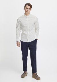 Weißes Hemd mit Stehkragen, kombiniert mit Navy-Hosen und hellbraunen Schuhen, aus weichem Stoff und in taillierter Passform.