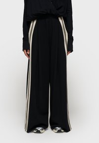 Zwarte wijde broek van zachte stof, met crèmekleurige zijstrepen langs de lengte en een elastische tailleband voor comfort.