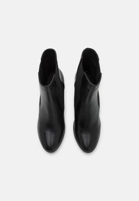 Botas de tornozelo em couro preto com um design elegante, textura suave, bicos arredondados e painéis laterais elásticos para facilitar o uso.