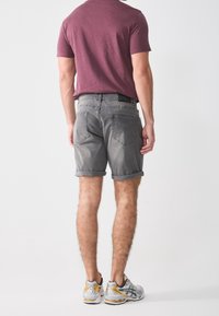 Shorts en denim gris avec ourlets retroussés, associés à un t-shirt bordeaux et des chaussures de sport grises et jaunes. Poches arrières visibles et détails de couture.