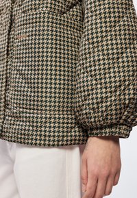 Prošívaná bunda ve vzoru zeleného a béžového psího zubu, s elastickými manžetami, bočními kapsami a měkkou texturou.