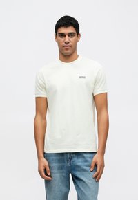 Ανοιχτό μπεζ κοντομάνικη μπλούζα με στρογγυλή λαιμόκοψη και μικρό μαύρο λογότυπο "Barbour International" στο στήθος. Απαλό βαμβακερό υλικό.