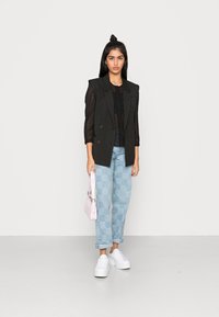 Blazer cruzado riscado a preto, sobre uma blusa preta, combinado com jeans azul claro xadrez, sapatilhas brancas de plataforma e uma pequena mala rosa.