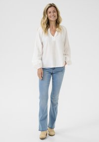 Løs-fittende hvid bluse med en blød tekstur, v-udskæring og puffede ærmer, parret med lys blå flagrende jeans og beige klipklapper.