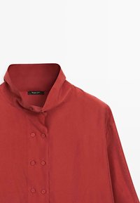 Rotes Hemd mit Knöpfen und Kragen, mit glatter Textur und sechs Knöpfen in zwei Reihen auf der Vorderseite. Markenlabel am Kragen sichtbar.