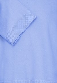 Tissu tricoté bleu clair avec poignets et ourlet côtelés, montrant les détails de texture et de couture d'une manche de pull.