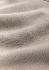 Gros plan d’un tissu beige doux avec une texture tissée fine et des plis subtils, montrant une surface lisse et uniforme.