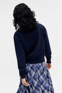 Dunkelblaues Sweatshirt mit langen Ärmeln und gerippten Bündchen, getragen mit einem karierten Rock in Blau-, Weiß- und Grautönen.