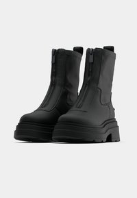 Mustad pahkluu saapad paksu taldiga, siledast materjalist, kahe külje tõmblukkidega ja tagaküljel aasadega mugavaks jalga panekuks.