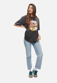 Svart oversized t-shirt med färggrafisk tecknad bild. Kombination med ljusblå raka jeans och gröna mockaskor.